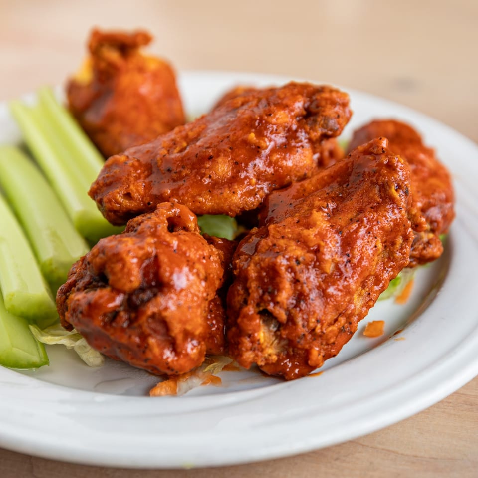 Spicy buffalo chicken wings with celery sticks and lettuce on a white plate.